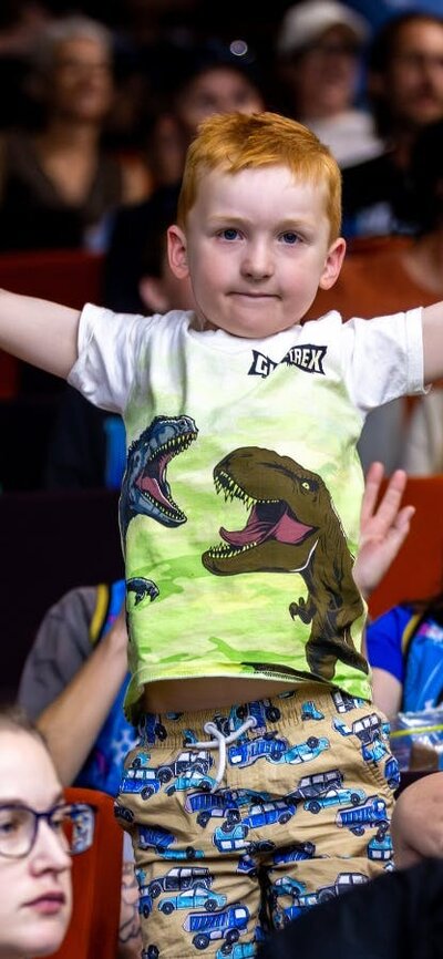 Child stands on a seat cheering and waving.