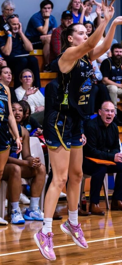 UC Capitals player Jayda Clark in the motion of shooting a 3 pointer with her teammates behind her.