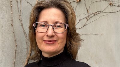 Claudia Craig A woman with brown, wavy hair and glasses, wearing a black turtleneck.