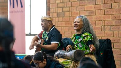 2 performers play music for an audience, one playing a guitar and one playing percussion instrument