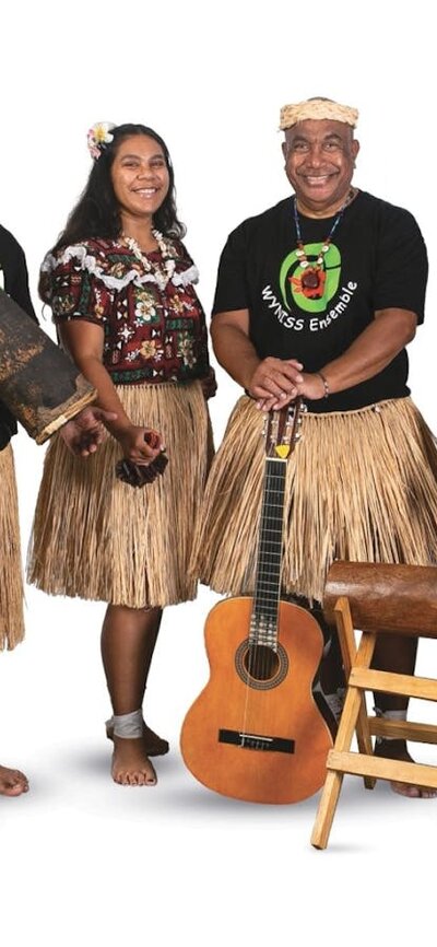4 musicians stand, wearing grass skirts, holding a guitar and wooden percussion instruments