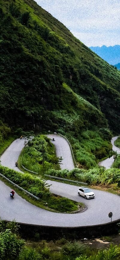 A windy road passes through green hills. In the background distant blue hills are visible