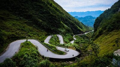 A windy road passes through green hills. In the background distant blue hills are visible